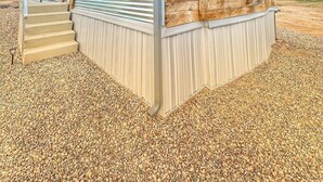 Une maison de plain-pied avec une façade en bois et un toit bleu, dotée d’un porche à l’avant et d’un escalier menant à l’entrée.