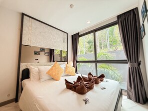 A hotel room with a bed, a large window, and a view of greenery outside.