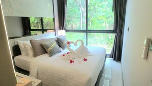 A hotel room with a large bed, white bedding, and a view of greenery through the window. - A206- 2 Bedroom Serviced Apartment with Forest View at Ao Nang Beach (Tambon Ao Nang)