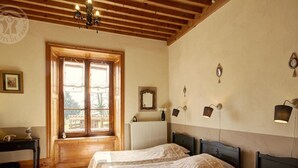 Habitación con dos camas, vigas de madera en el techo, ventana con vistas, radiador y lámparas de pared.