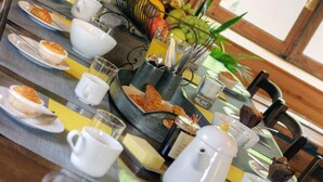 Un desayuno con platos de comida, tazas, una cesta de frutas y una jarrón.