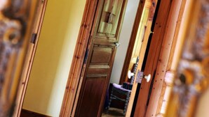 Un pasillo con puertas de madera y vista a una habitación con una silla y una mesita.