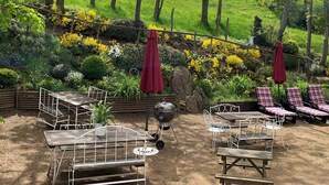Un patio al aire libre con mesas y sillas de metal, rodeado por un jardín con diversas plantas y flores.