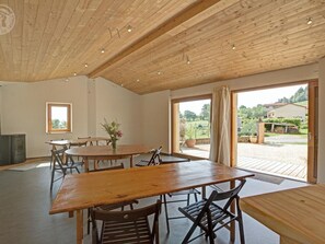 Una habitación amplia con techo de madera, ventanas grandes y una zona de comedor con mesas y sillas de madera.