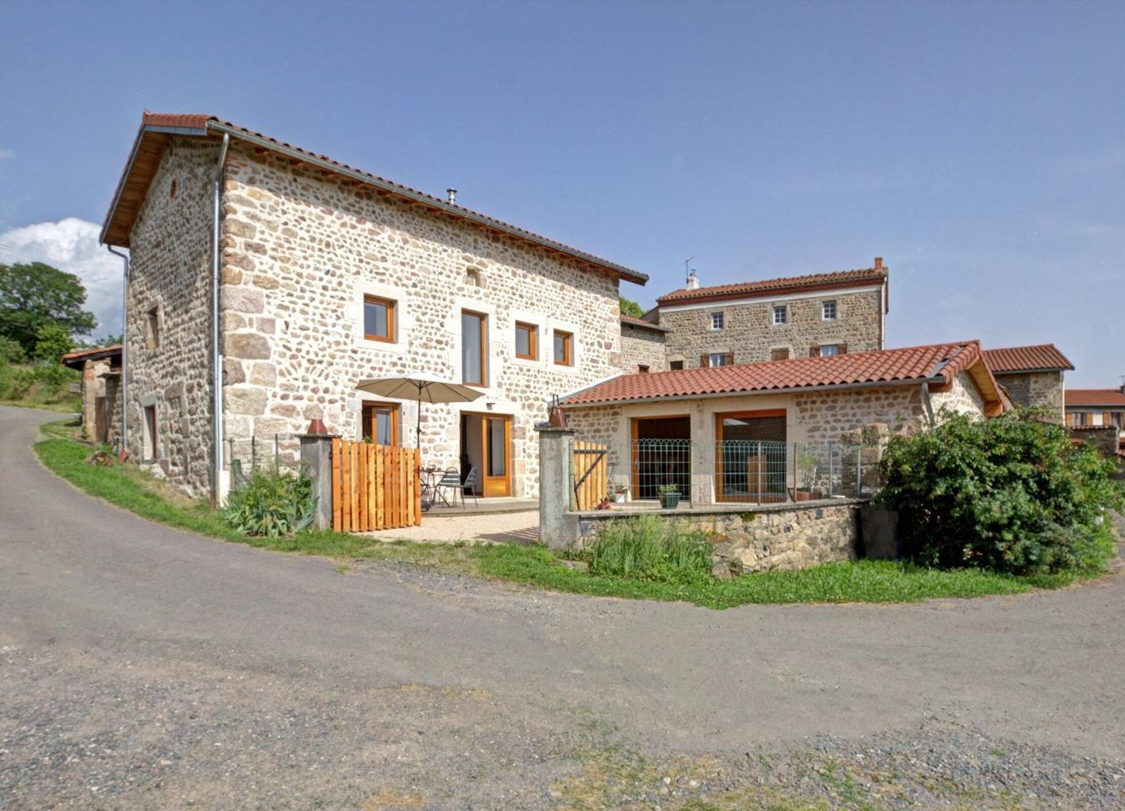 A stone building with a small attached structure, a paved driveway, and a wooden fence.