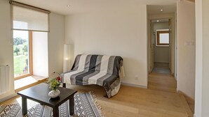 A bedroom with a bed, a bedside table with a vase, a window with blinds, and a hallway leading to another room. - Renovated traditional farmhouse with private courtyard in Verrières-en-Forez (Verrières-en-Forez)