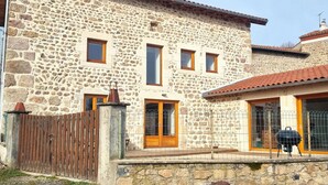A stone building with a wooden door and windows, a fenced area, and a barbecue grill. - Renovated traditional farmhouse with private courtyard in Verrières-en-Forez (Verrières-en-Forez)