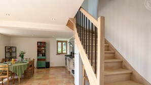 A spacious living area with a dining table, chairs, a bookshelf, and a kitchen area with a staircase. - Renovated traditional farmhouse with private courtyard in Verrières-en-Forez (Verrières-en-Forez)