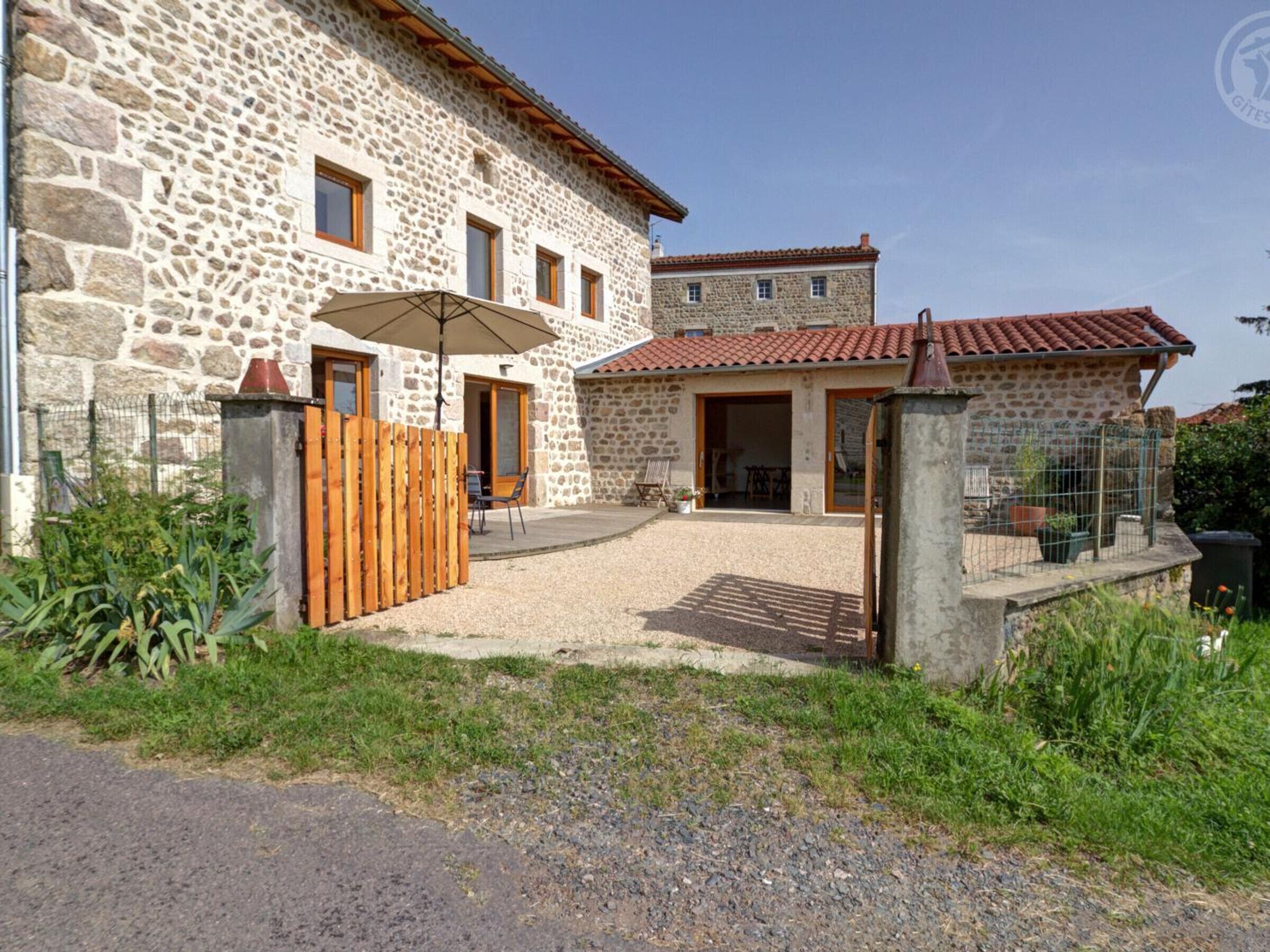 A stone building with a gravel driveway, wooden fence, and a patio area with outdoor furniture.