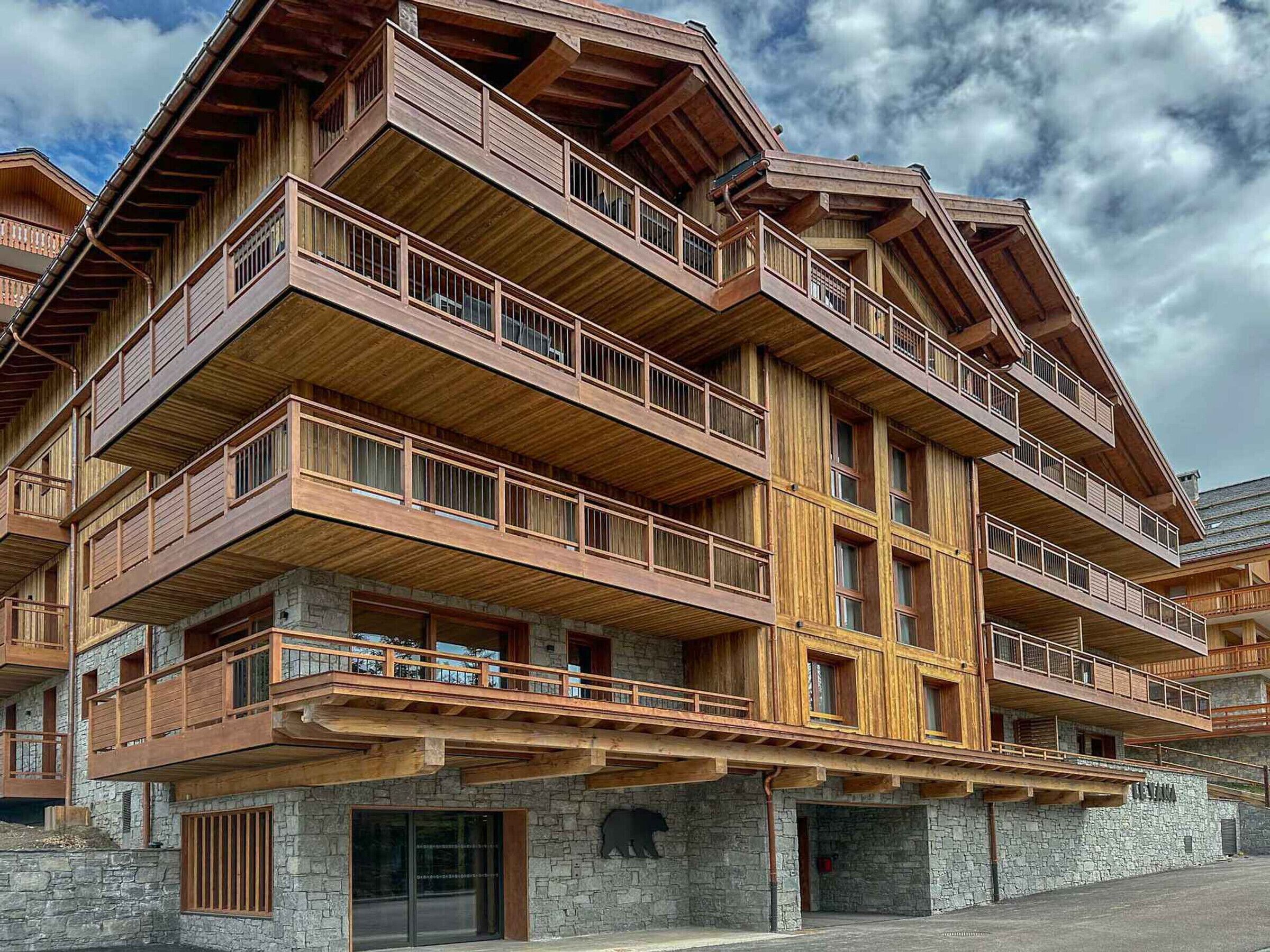 Una cabaña de madera de varios pisos con balcones, paredes de piedra y una escultura de oso.
