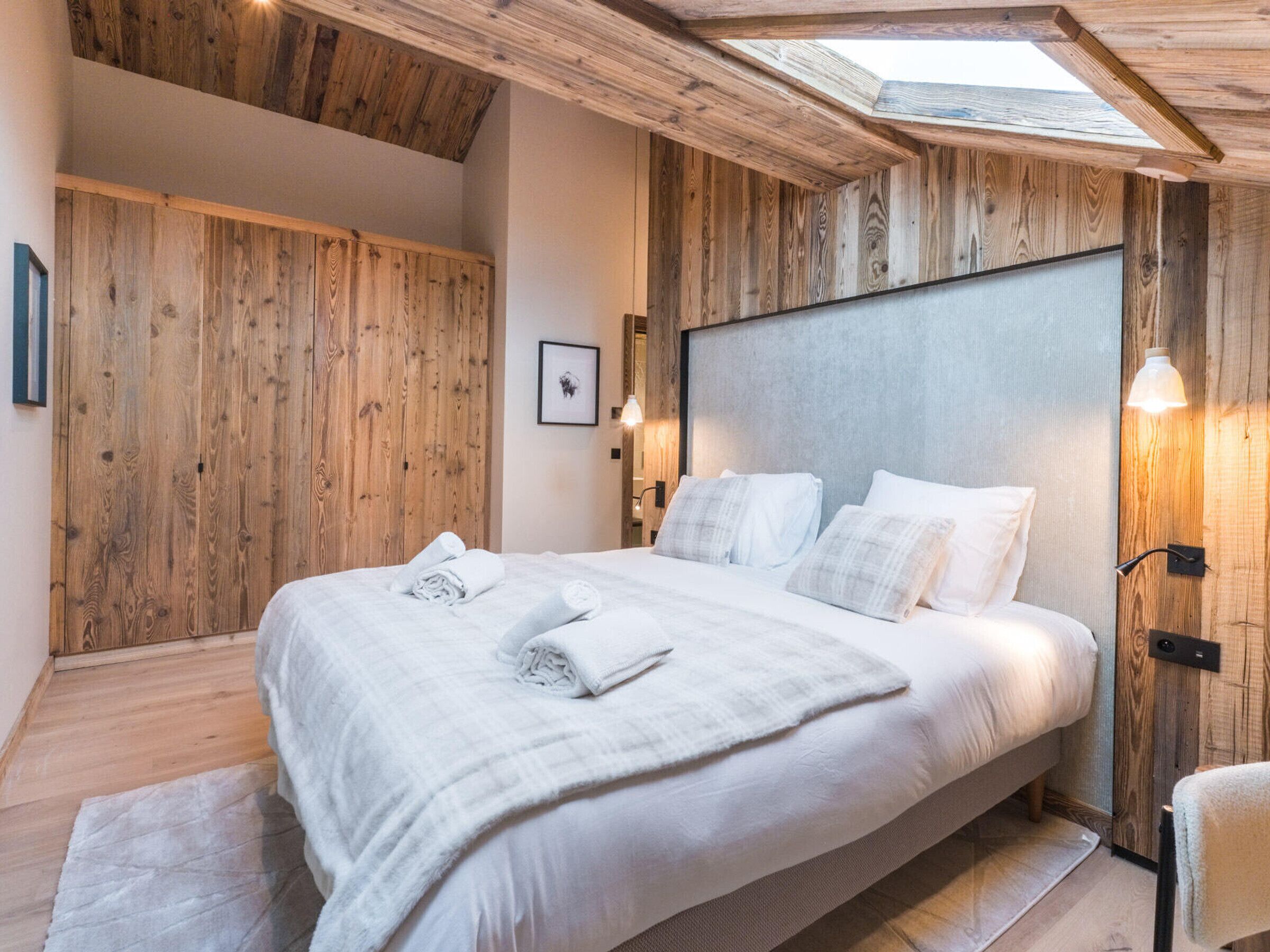 A bedroom with a large bed, wooden walls, and a skylight.