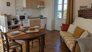 Een gezellige woonkamer met een houten eettafel, een bank en een keuken met een magnetron en kastjes.