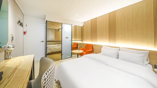Una habitación de hotel moderna con una cama grande, un escritorio, una silla y una mesita. Hay un espejo y una puerta que da al baño.