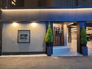 A hotel entrance with a sign reading "No.25 HOTEL", two potted plants, and a parking garage in the background. - NO.25 Hotel Dongam (Incheon)