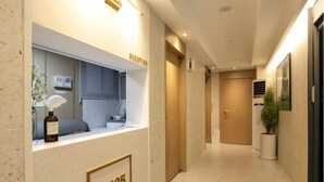 Zona de recepción de un hotel, con mostrador de recepción, un área de estar y un pasillo que conduce a una puerta.