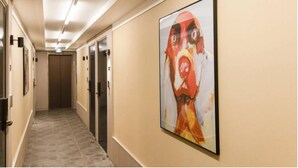 Un pasillo de hotel con un cuadro abstracto grande en la pared, puertas y suelo de baldosas.