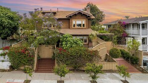 A two-story house with a front porch, a staircase leading to the entrance, and a small front yard with various plants and flowers. - Spacious 6BR near Balboa Park with hot tub, game room & room for 15 - perfect for families or groups (San diego)