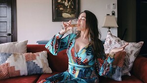 Uma pessoa sentada em um sofá vermelho com almofadas estampadas, vestindo um vestido colorido.