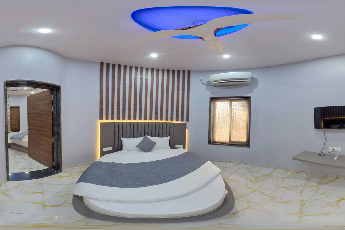 Ein modernes Schlafzimmer mit einem gewölbten Bett, einem Deckenventilator, Einbauleuchten, einer Wand-Klimaanlage, einem Fernseher und einem Nachttisch.