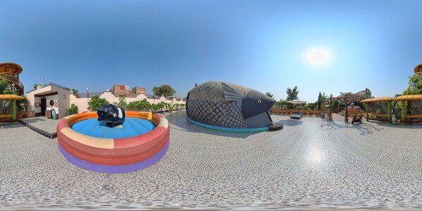 Un parc aquatique doté d’une grande baleine gonflable, d’un toboggan aquatique circulaire et d’une zone aménagée avec des parasols et des sièges.