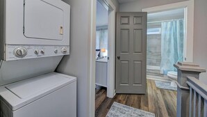A laundry room with a front-loading washer and dryer, a door leading to a bathroom with a shower and toilet.