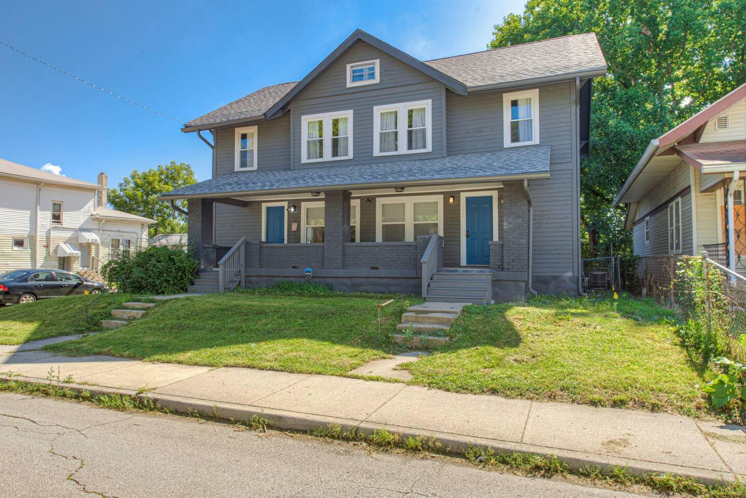 A two-story house with a front porch, a small front yard, and a driveway.