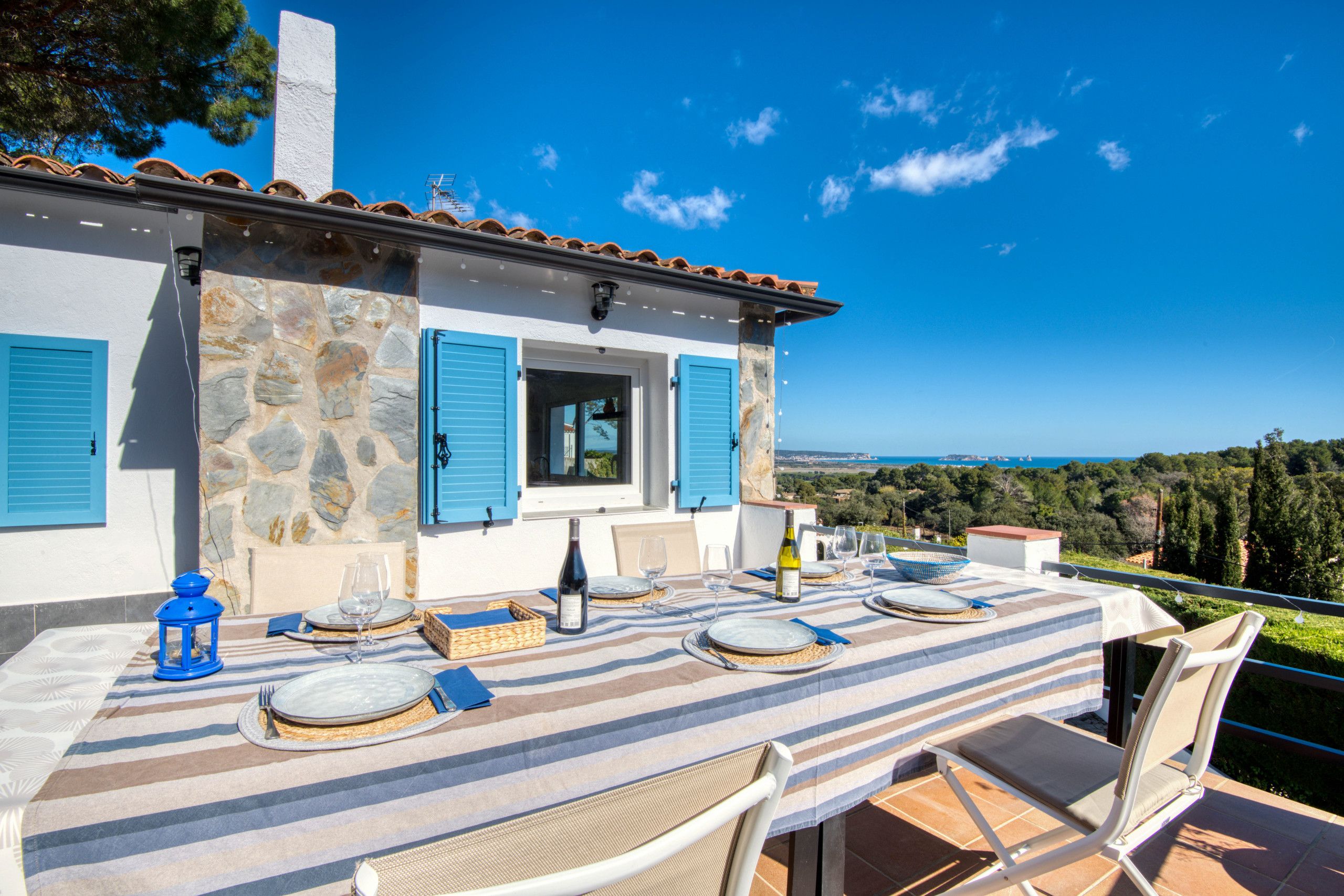 A dining table set with plates, glasses, and a bottle, overlooking a scenic landscape.