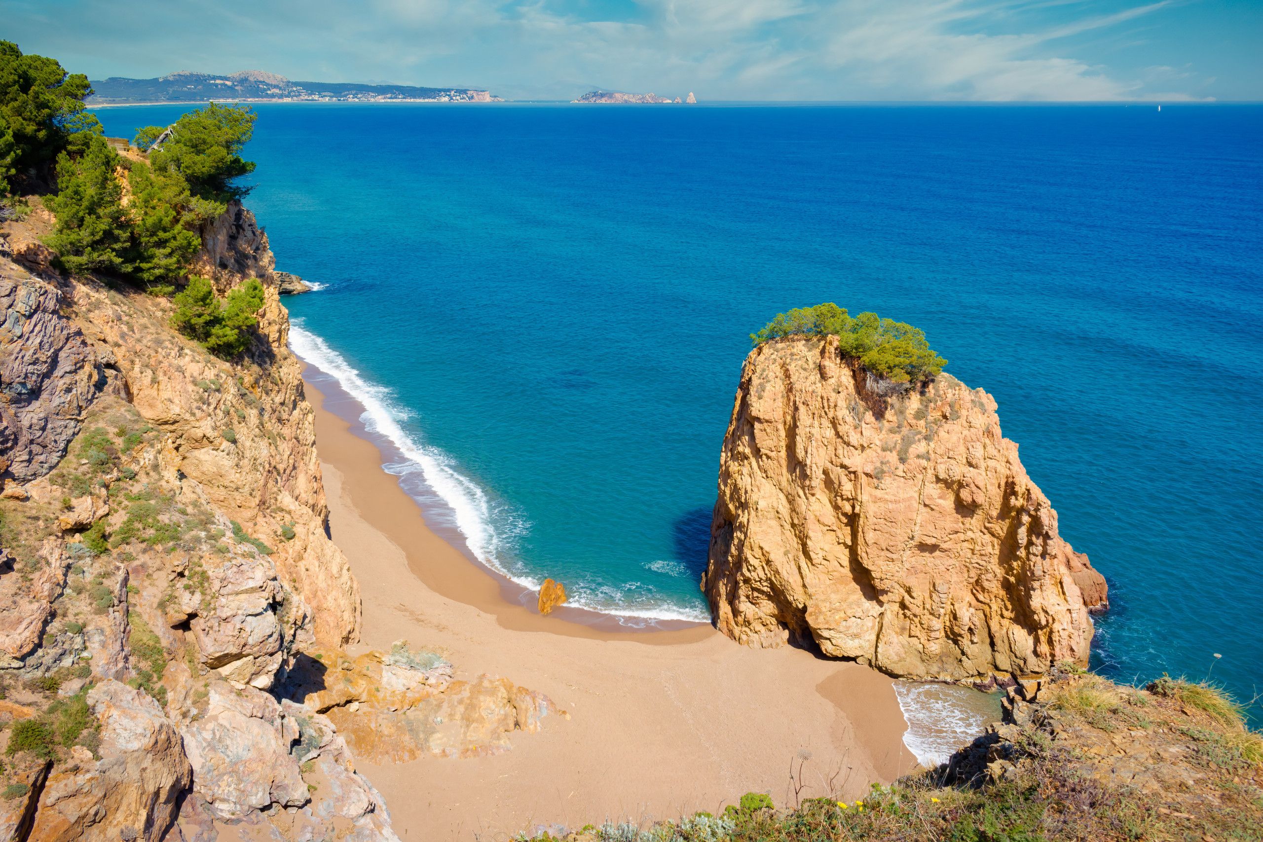 A coastal landscape with a rocky cliff, a sandy beach, and a clear blue sea.
