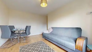 Un salon moderne avec un canapé gris, une table à manger avec des chaises et un tapis à motifs.