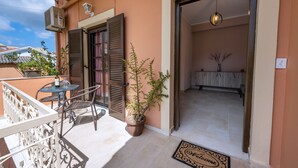 A balcony with a table and chairs, a potted plant, and a door leading to an interior space with a tiled floor and a hanging light fixture. - La Casa di Volpe (Corfu)