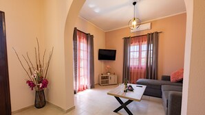 A living room with a sofa, a coffee table, a flat-screen TV, and a vase of flowers. - La Casa di Volpe (Corfu)