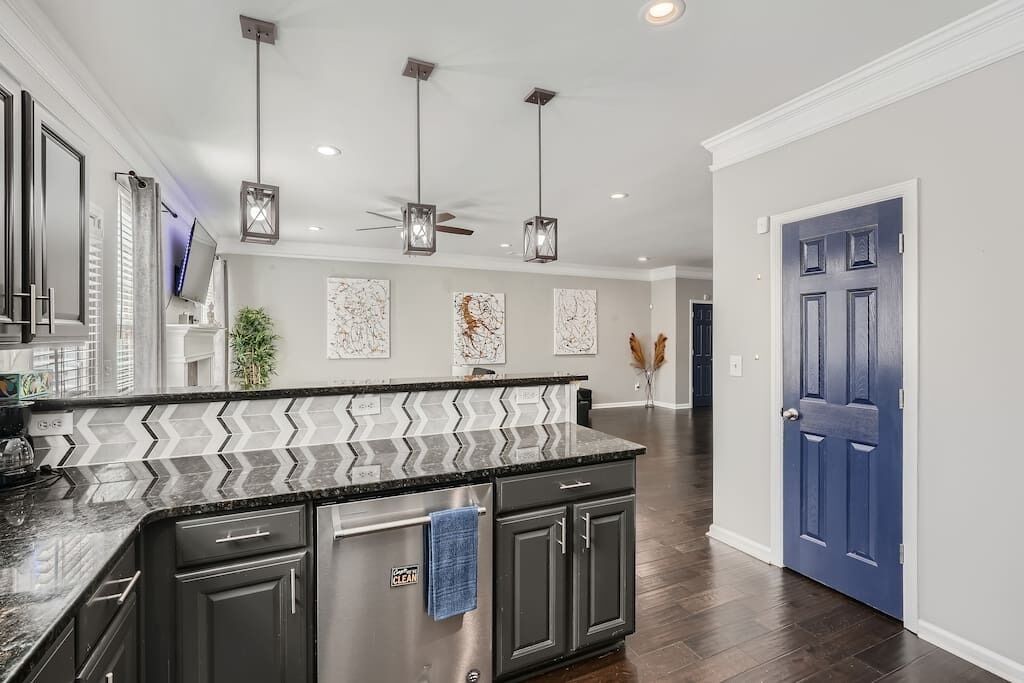 A modern kitchen with a black granite countertop, stainless steel appliances, and pendant lighting.