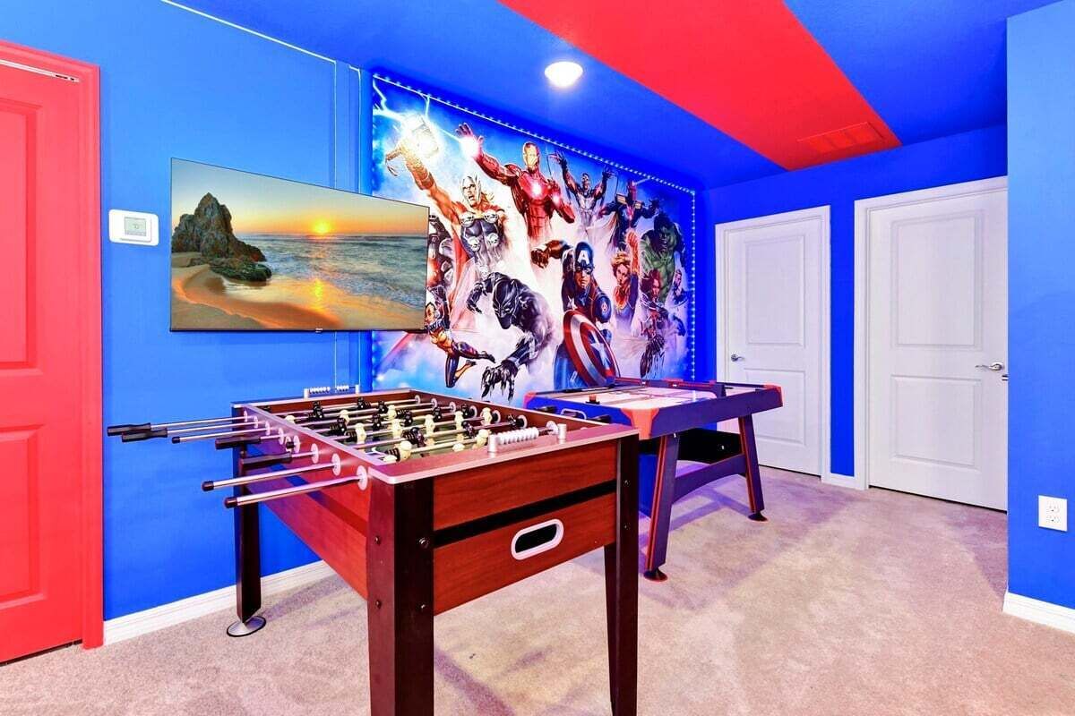 Una habitación con una mesa de fútbol de mesa, un cuadro de una puesta de sol y un mural de superhéroes.