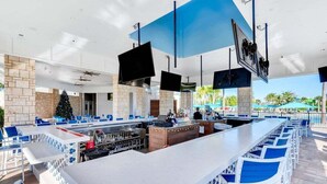 An outdoor bar area with a long counter, blue chairs, and a Christmas tree.