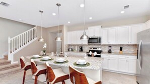 A modern kitchen with white cabinets, granite countertops, stainless steel appliances, and pendant lighting.