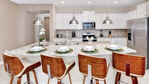 A modern kitchen with white cabinets, a central island with bar stools, stainless steel appliances, and pendant lighting.