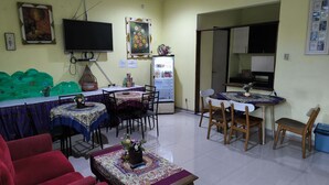 A dining area with a table and chairs, a refrigerator, and a television mounted on the wall. - Promosia Guest House (Surabaya)