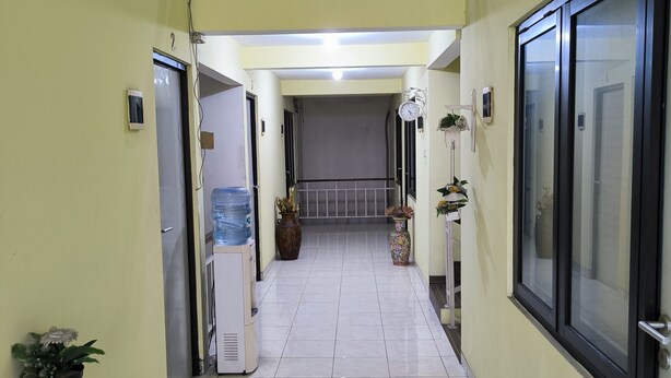 A corridor with a water dispenser, potted plants, and a ceiling fan. - Promosia Guest House (Surabaya)