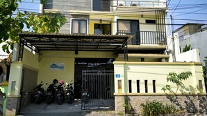 A two-story residential building with a gated entrance, a covered parking area, and a sign indicating the property name. - Promosia Guest House (Surabaya)