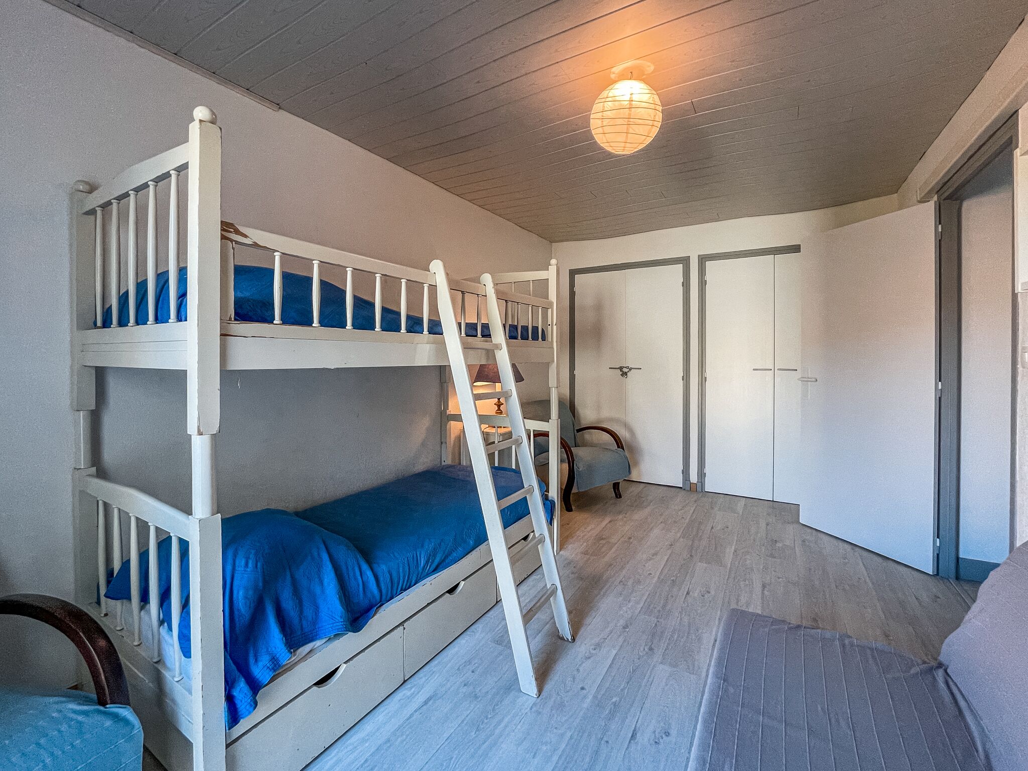 Een slaapkamer met een stapelbed, een ladder, een stoel en een bureau. Er zijn twee deuren en een raam.