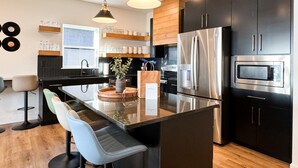 Une cuisine moderne dotée d’un îlot central, d’appareils électroménagers en acier inoxydable et de meubles de rangement noirs.
