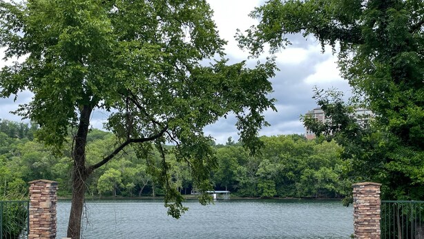 A swimming pool with stone pillars, surrounded by lush greenery and a lake.