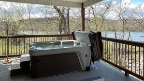 A hot tub on a wooden deck with a view of a lake and trees.