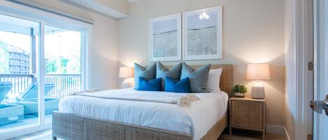 A bedroom with a large bed, two bedside tables, a view to a balcony, and two wall-mounted artworks.