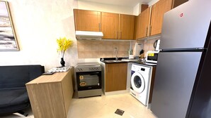 A compact kitchen with wooden cabinets, a built-in oven, a washing machine, and a refrigerator. - Cosmos Living Stunning Apt in Lago Vista (Dubai)