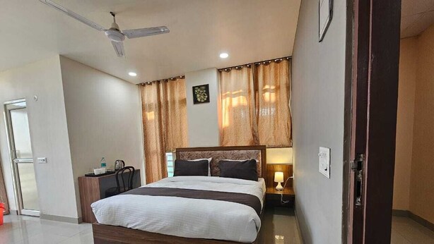 A modern hotel room with a large bed, a bedside table, a nightstand, a ceiling fan, and a door. - Hotel Vistacrest Noida Sector 104 (Noida)