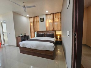 A modern hotel room with a large bed, a bedside table, a nightstand, a ceiling fan, and a door.