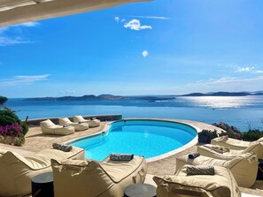 Ein Poolbereich mit Liegestühlen und Blick auf das Meer.