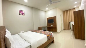 A hotel room with a bed, a TV mounted on a wooden panel, a ceiling fan, and a door with curtains. - Hotel Vistacrest Noida Sector 35 (Noida)