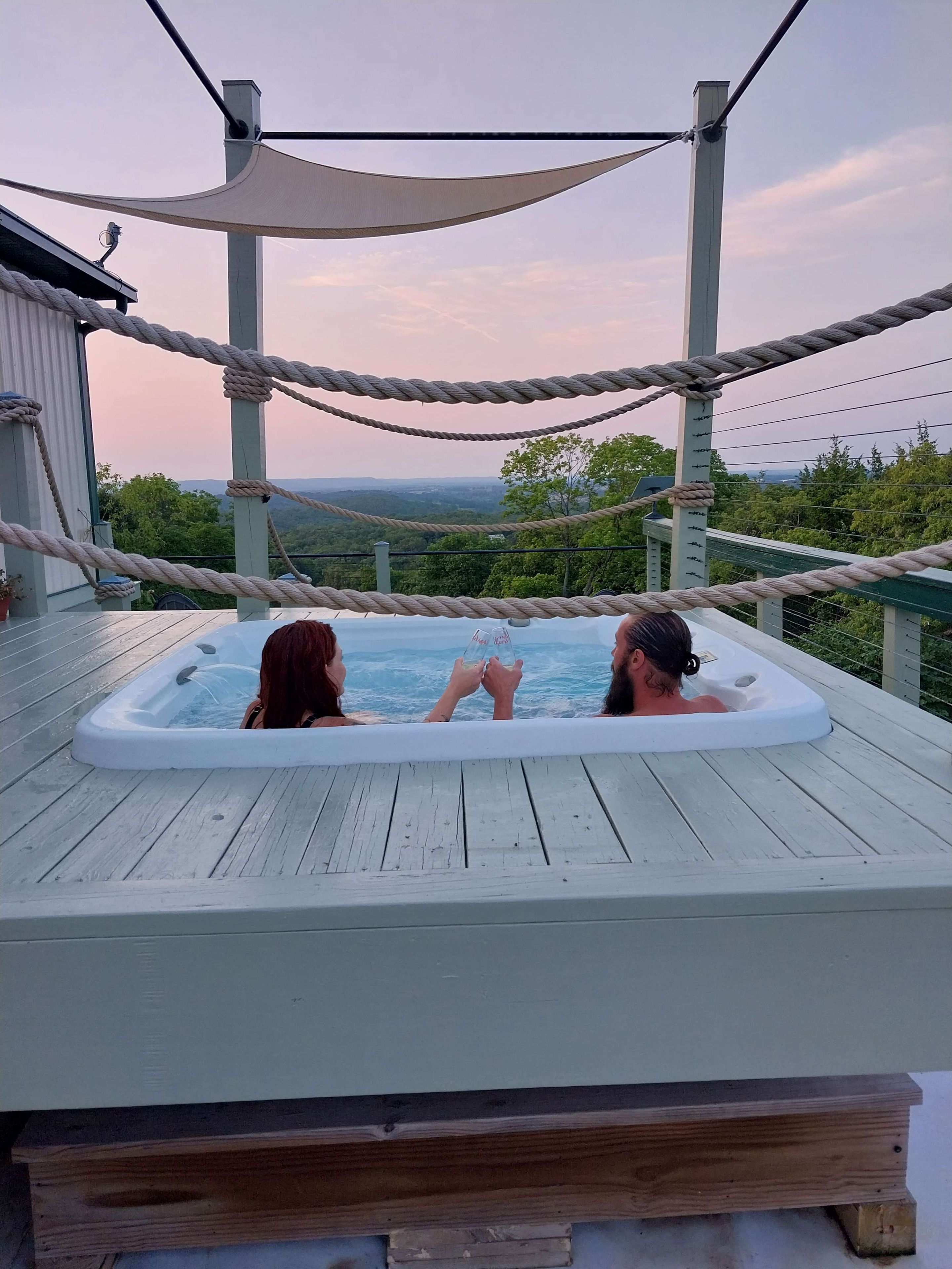 Un bain à remous sur une terrasse en bois, délimité par une barrière en corde, avec vue sur le paysage.